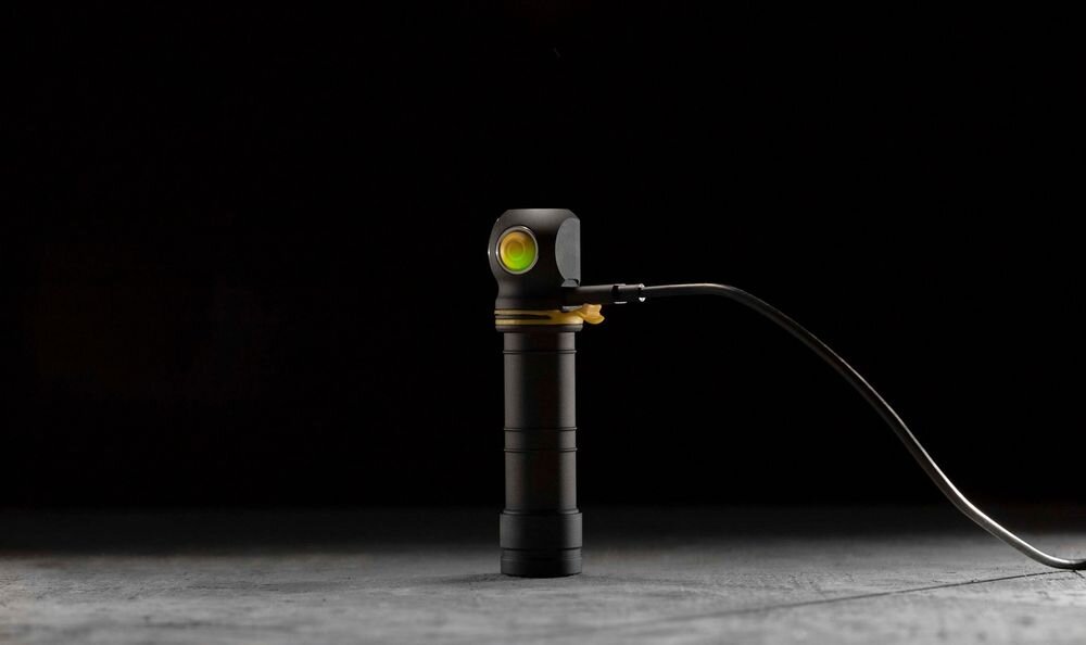 Latarka ARMYTEK F10702PC Elf C2 Max LR Czarny, latarka, jasność, akumulator, zasilanie, Czarna latarka kątowa stojąca w pionie na jasnym podłożu, podłączona do kabla ładującego.