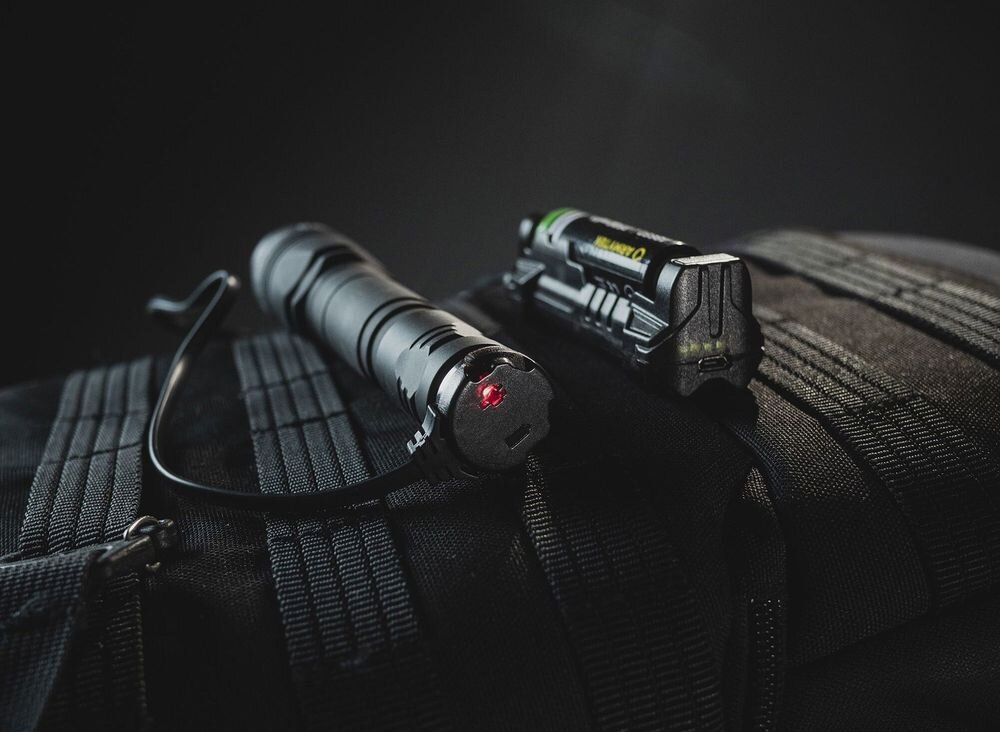 Ładowarka do latarek taktycznych ARMYTEK A05003 AMC-03, kabel, ładowarka, zasilanie, magnes, Ładowanie latarki taktycznej leżącej na plecaku.