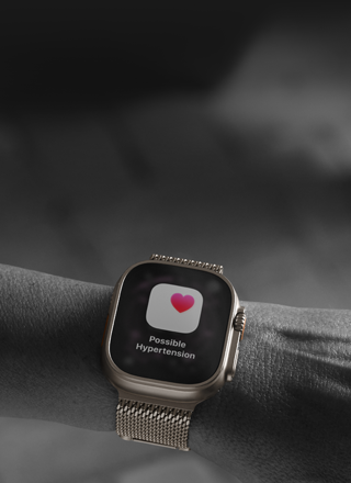 Na zdjęciu widoczny jest smartwatch na nadgarstku, z wyświetlaczem pokazującym ikonę serca i tekst \'Possible Hypertension\'.