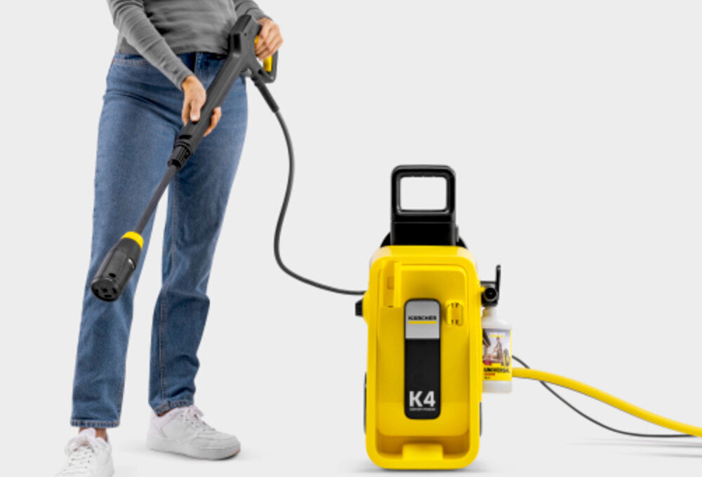 Osoba trzymająca lancę myjki ciśnieniowej obok żółtej myjki z napisem \'K4\' i logo \'KARCHER\'.