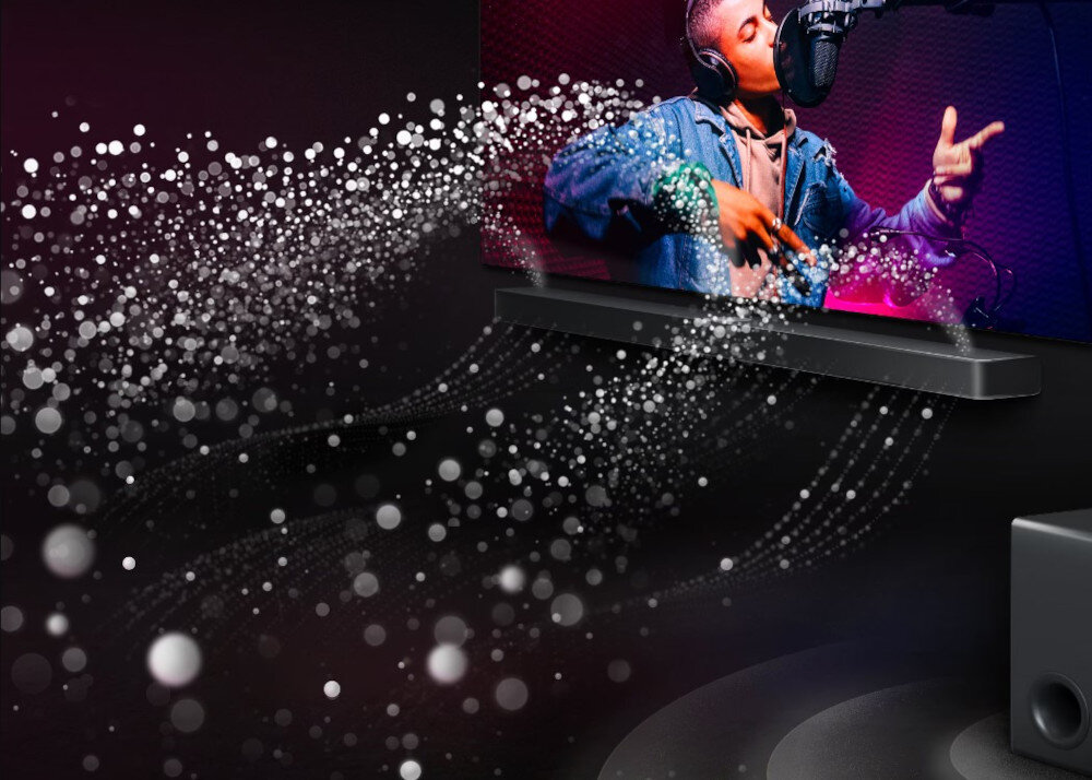 Obraz przedstawia soundbar umieszczony pod ekranem, na którym widać osobę śpiewającą do mikrofonu. Wokół soundbara widoczne są efekty wizualne przypominające fale dźwiękowe z białymi kropkami.