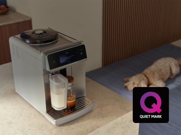 Ekspres do kawy z wyświetlaczem, przygotowujący kawę z mlekiem i espresso. Obok ekspresu znajduje się logo \'Quiet Mark\'.