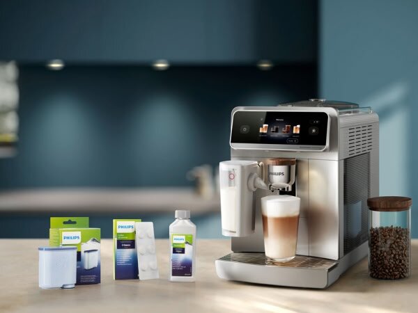 Na obrazie znajduje się ekspres do kawy z filiżanką kawy z mleczną pianką. Obok ekspresu widoczne są opakowania z akcesoriami i środkami czyszczącymi marki Philips oraz pojemnik z ziarnami kawy.