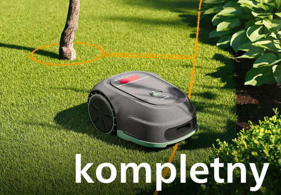 Robot koszący na trawie z pomarańczową linią wokół drzewa. Na dole widoczny jest napis \'kompletny\'.