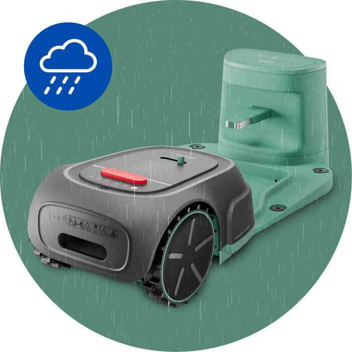 Na obrazie znajduje się robot koszący w kolorze szarym z zielonymi elementami, stojący na stacji dokującej. W lewym górnym rogu widoczna jest ikona chmury z deszczem na niebieskim tle.