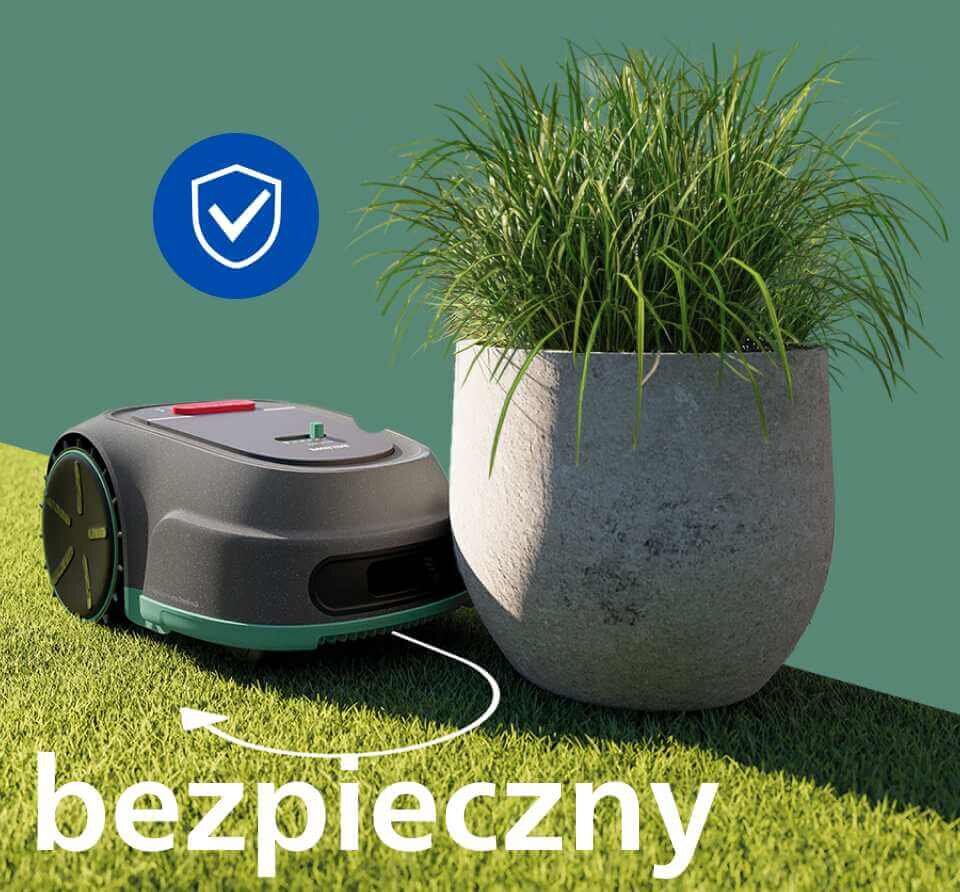 Robot koszący obok donicy z trawą na tle zielonej trawy. Na obrazie widoczny jest niebieski symbol tarczy z białym haczykiem oraz napis \'bezpieczny\'.