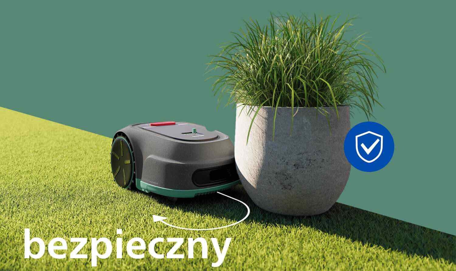 Robot koszący znajduje się na trawie obok donicy z rośliną. Na obrazie widoczny jest napis \'bezpieczny\' oraz niebieska ikona z symbolem tarczy i haczyka.
