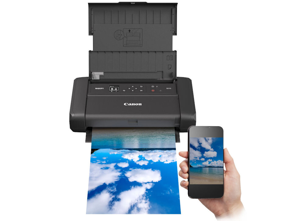 Drukarka Canon z otwartą pokrywą, drukująca kolorowe zdjęcie przedstawiające plażę i niebo. Obok widoczna jest ręka trzymająca smartfon z tym samym zdjęciem na ekranie.