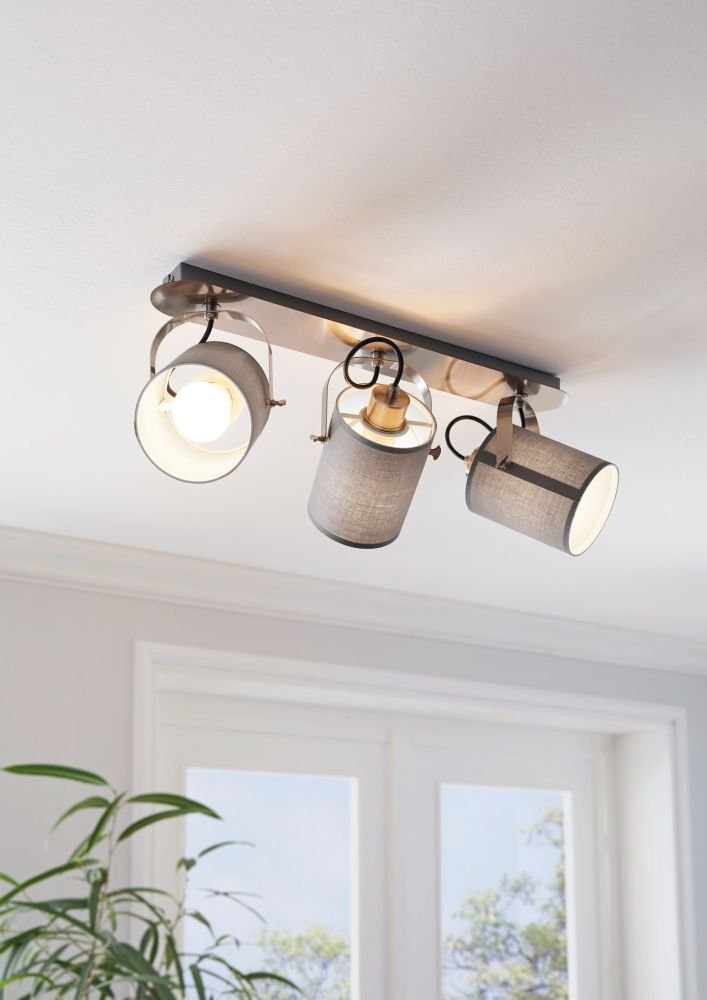 Na suficie zamontowana jest lampa reflektorowa z trzema szarymi kloszami, z których jeden jest włączony. W tle widoczne są okna i fragment rośliny.