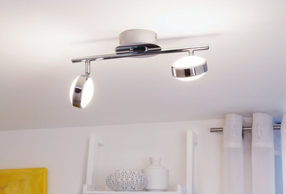 Na obrazie widoczna jest lampa reflektorowa z dwoma źródłami światła zamontowana na suficie. W tle znajdują się zasłony i półka z dekoracjami.
