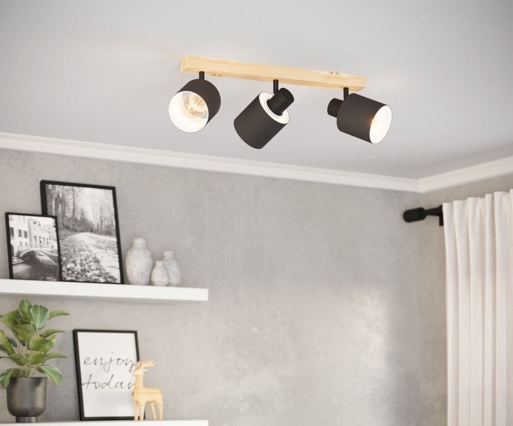 Na suficie zamontowana jest lampa reflektorowa z trzema czarnymi kloszami na drewnianej listwie. Na ścianie poniżej znajdują się półki z dekoracjami, w tym rośliną i zdjęciami, a na jednej z nich widoczny jest napis \'enjoy today\'.