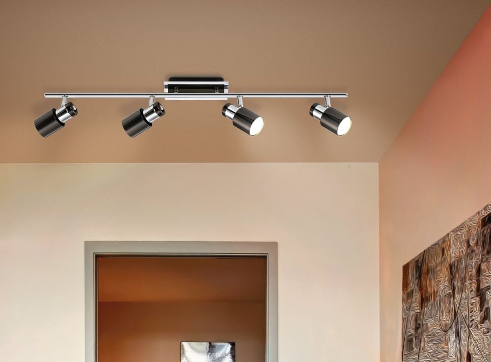 Na obrazie widoczna jest lampa sufitowa z czterema regulowanymi reflektorami w metalicznym wykończeniu. Lampa zamontowana jest na suficie w pomieszczeniu z jasnymi ścianami i ozdobnym obrazem na ścianie.