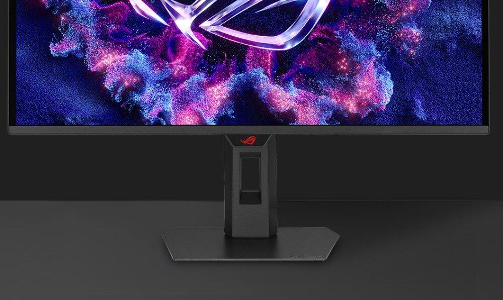 Monitor z cienką ramką, wyświetlający kolorową grafikę z logo producenta na środku. Podstawa monitora jest czarna z czerwonym logo producenta.