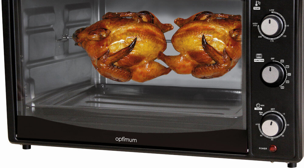Mini piekarnik z logo \'optimum\' na drzwiczkach, w środku pieką się dwa kurczaki na rożnie. Panel sterowania z pokrętłami do regulacji temperatury, funkcji i czasu znajduje się z boku.