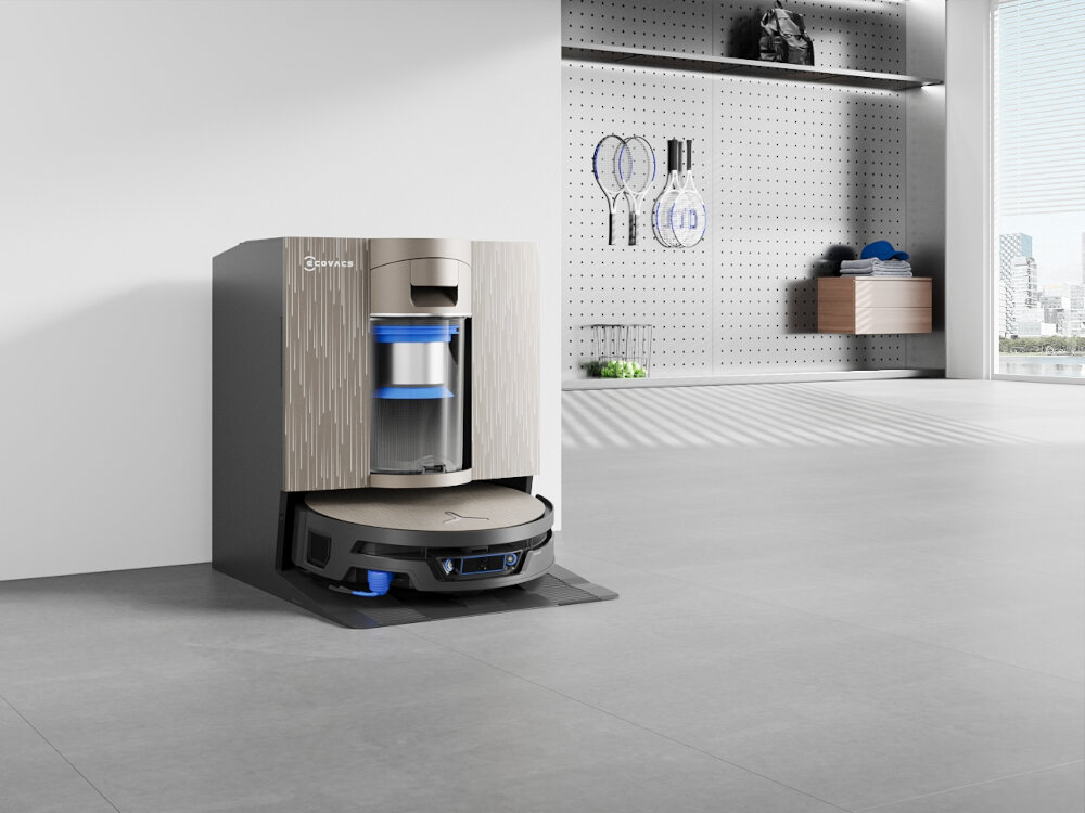 Robot sprzątający znajduje się w stacji dokującej w nowoczesnym wnętrzu. Na stacji widoczne jest logo \'ECOVACS\'.