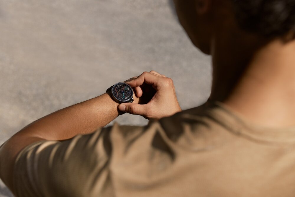 Osoba patrzy na czarny smartwatch na swoim nadgarstku. Tło jest rozmyte i jednolite.