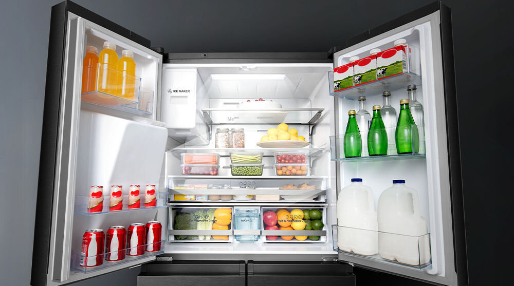 Otwarta lodówka z widocznymi półkami wypełnionymi różnymi produktami spożywczymi, takimi jak napoje, owoce i warzywa. Na drzwiach lodówki znajduje się logo \'ICE MAKER\'.