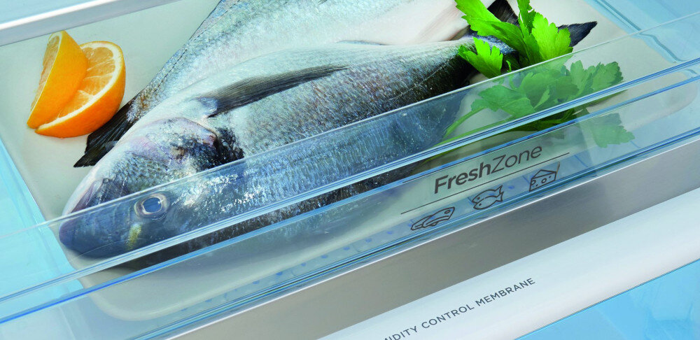 Wnętrze lodówki z szufladą oznaczoną jako \'FreshZone\', w której znajduje się ryba, plasterki pomarańczy i zielone liście. Na szufladzie widoczny jest napis \'HUMIDITY CONTROL MEMBRANE\'.