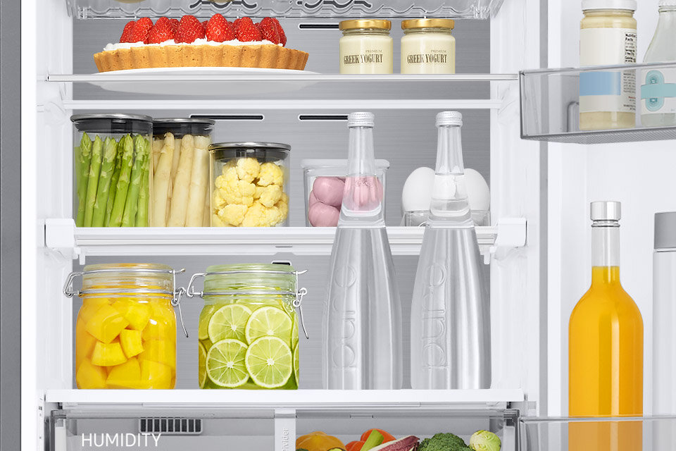 łatwo pomieścisz wysokie produkty Wnętrze lodówki z różnorodnymi produktami spożywczymi, w tym słoikami z owocami i warzywami, butelkami oraz ciastem na górnej półce. Widoczny napis \'HUMIDITY\' na jednej z półek.