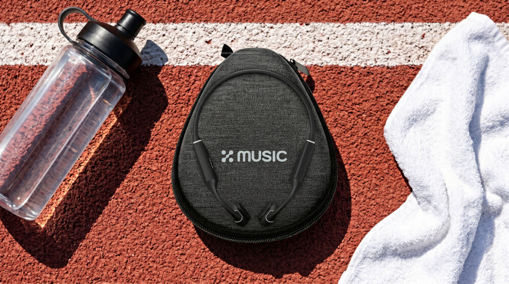 Na bieżni leży czarny futerał z logo \'XMUSIC\', obok przezroczysta butelka z wodą i biały ręcznik.