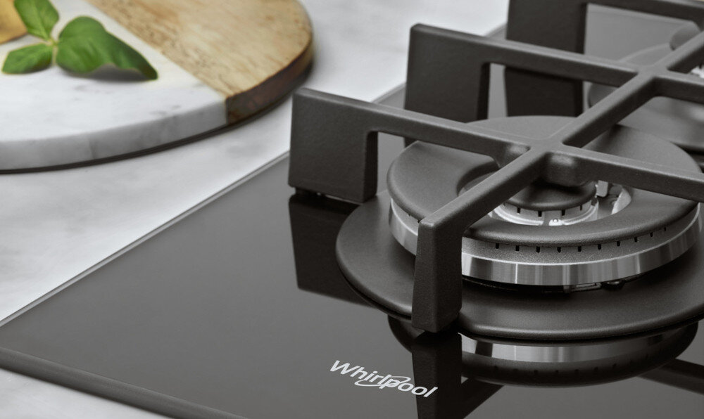 Czarna płyta gazowa z metalowym palnikiem i żeliwnym rusztem. Na powierzchni widoczne jest logo \'Whirlpool\'.