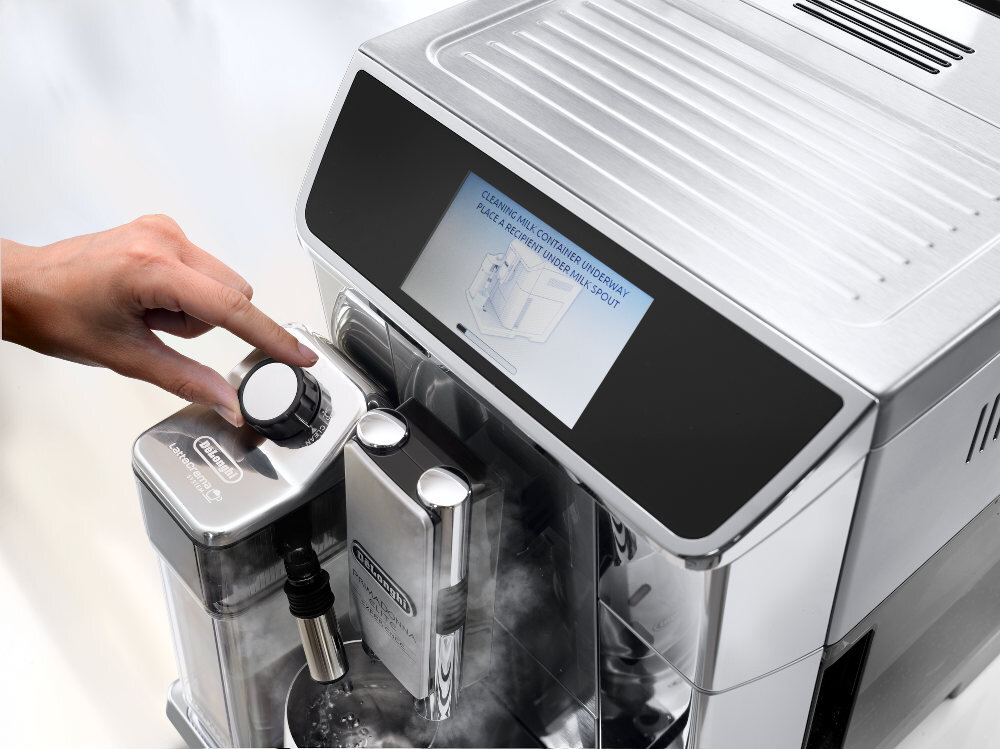 Osoba obsługuje ekspres do kawy, regulując pokrętło na panelu z logo \'DeLonghi\'. Na wyświetlaczu widoczny jest tekst: \'CLEANING MILK CONTAINER UNDERWAY PLACE A RECIPIENT UNDER MILK SPOUT\'.