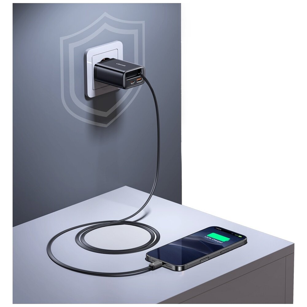 Ładowarka sieciowa podłączona do gniazdka ściennego z dwoma portami USB, do której podłączony jest kabel ładujący smartfon leżący na blacie. Na ekranie smartfona widoczny jest wskaźnik ładowania baterii.