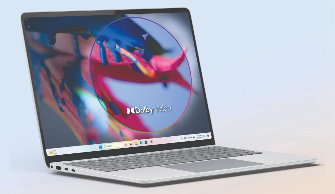 Laptop z wyświetlaczem prezentującym kolorową grafikę oraz logo \'Dolby Vision\'. Klawiatura jest widoczna, a na ekranie znajduje się pasek z ikonami systemu Windows.