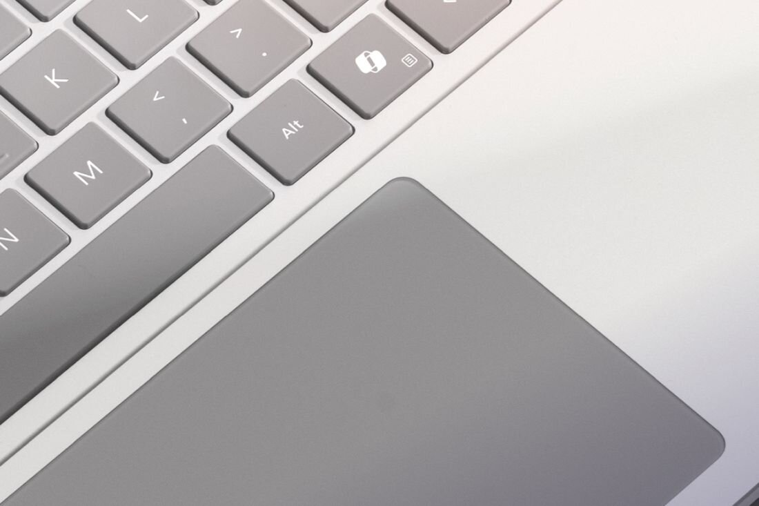 Zbliżenie na klawiaturę laptopa z widocznymi klawiszami, w tym \'Alt\' i klawisz z ikoną kłódki, oraz touchpad w szarym kolorze.