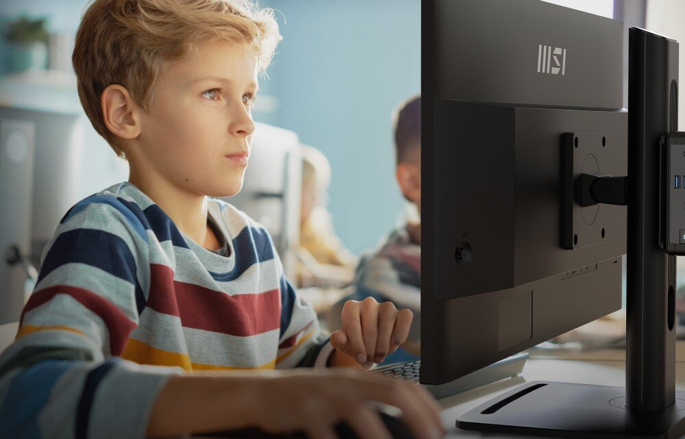 Osoba siedzi przed monitorem z logo MSI, używając klawiatury. Monitor jest zamontowany na regulowanym ramieniu.