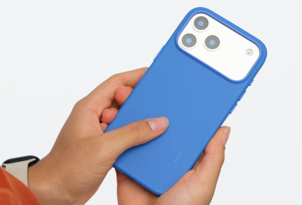 Osoba trzyma niebieskie etui na telefon z trzema widocznymi obiektywami aparatu. Na etui widoczny jest napis \'MOFT\'.
