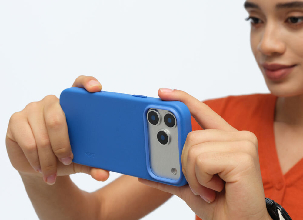 Osoba trzyma niebieskie etui na telefon z trzema widocznymi obiektywami aparatu. Na etui widoczny jest napis \'MOFT\'.