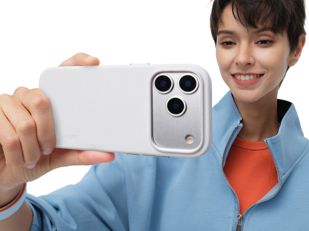 Osoba trzyma telefon w szarym etui z trzema widocznymi obiektywami aparatu. Na etui widoczne jest logo \'MOFT\'.