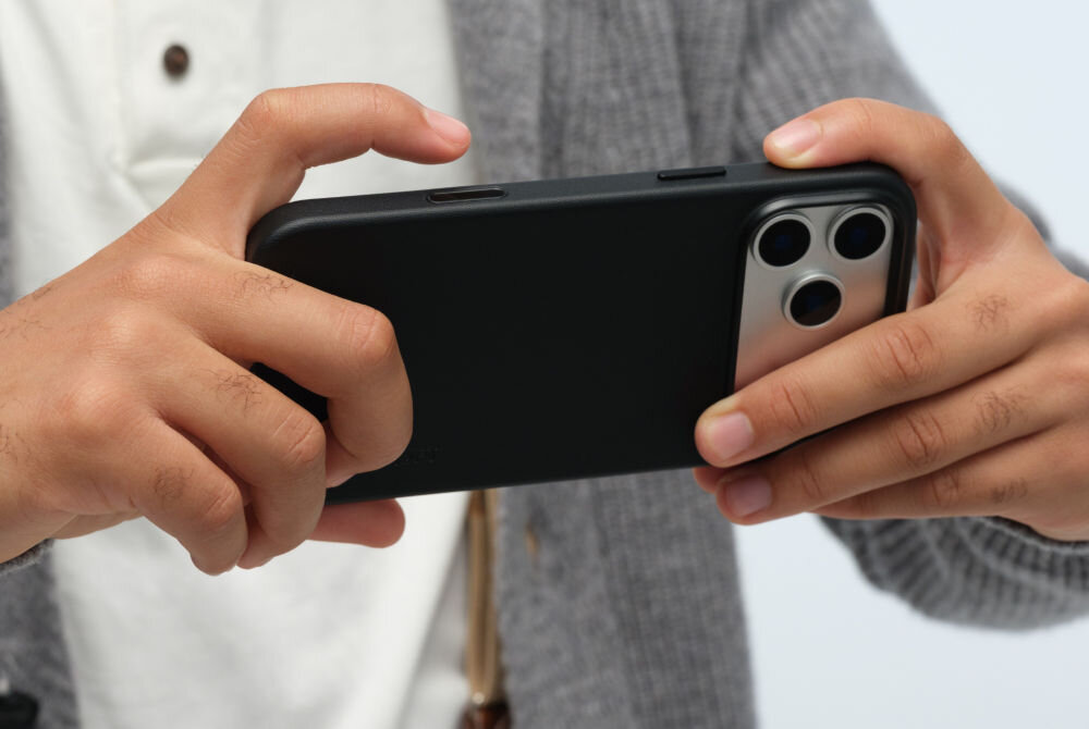 Osoba trzyma czarny telefon w etui, widoczne są trzy obiektywy aparatu z tyłu urządzenia.