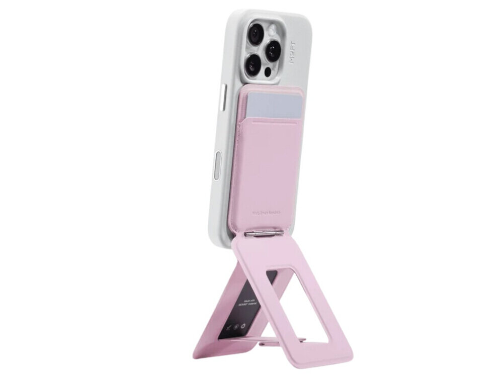 Na obrazie widoczny jest telefon z białą obudową, do którego przymocowany jest różowy magnetyczny portfel i stojak. Na portfelu znajduje się napis \'moft.com\'.