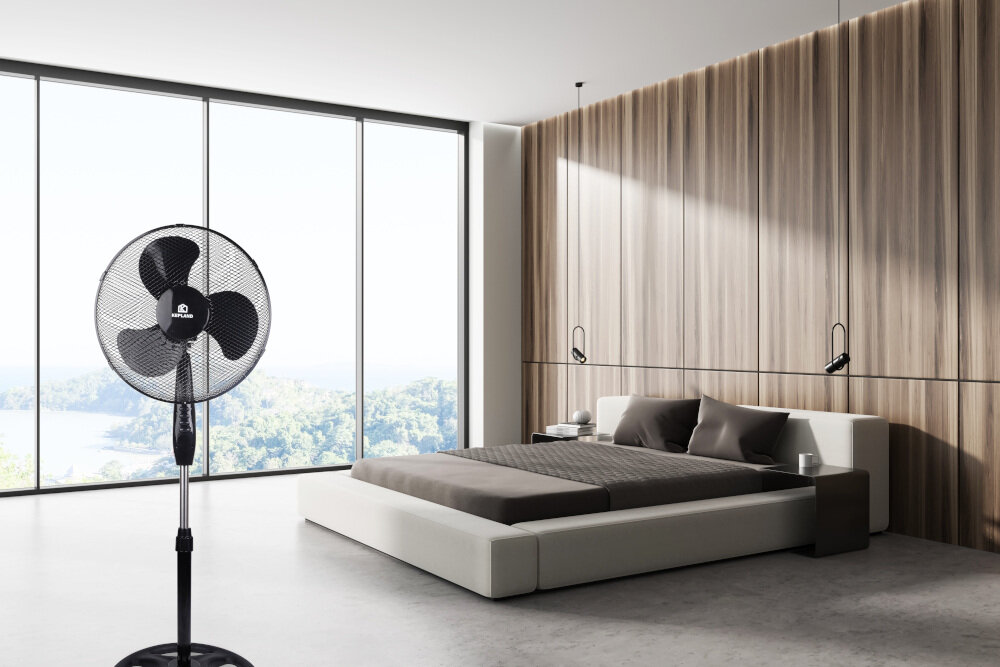 W nowoczesnej sypialni z dużymi oknami znajduje się czarny wentylator stojący z logo KEPLAND. Obok stoi niskie łóżko z szarymi i brązowymi poduszkami oraz drewniana ściana z lampami wiszącymi.