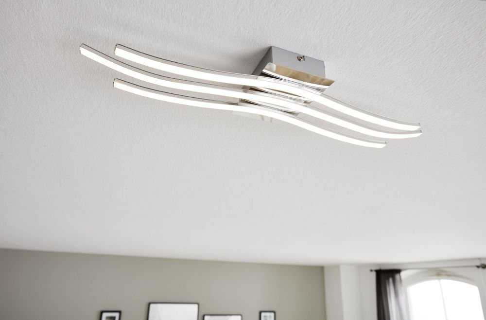 Na obrazie widoczna jest nowoczesna lampa sufitowa LED z czterema zakrzywionymi ramionami emitującymi światło. Lampa zamontowana jest na białym suficie w jasnym pomieszczeniu.