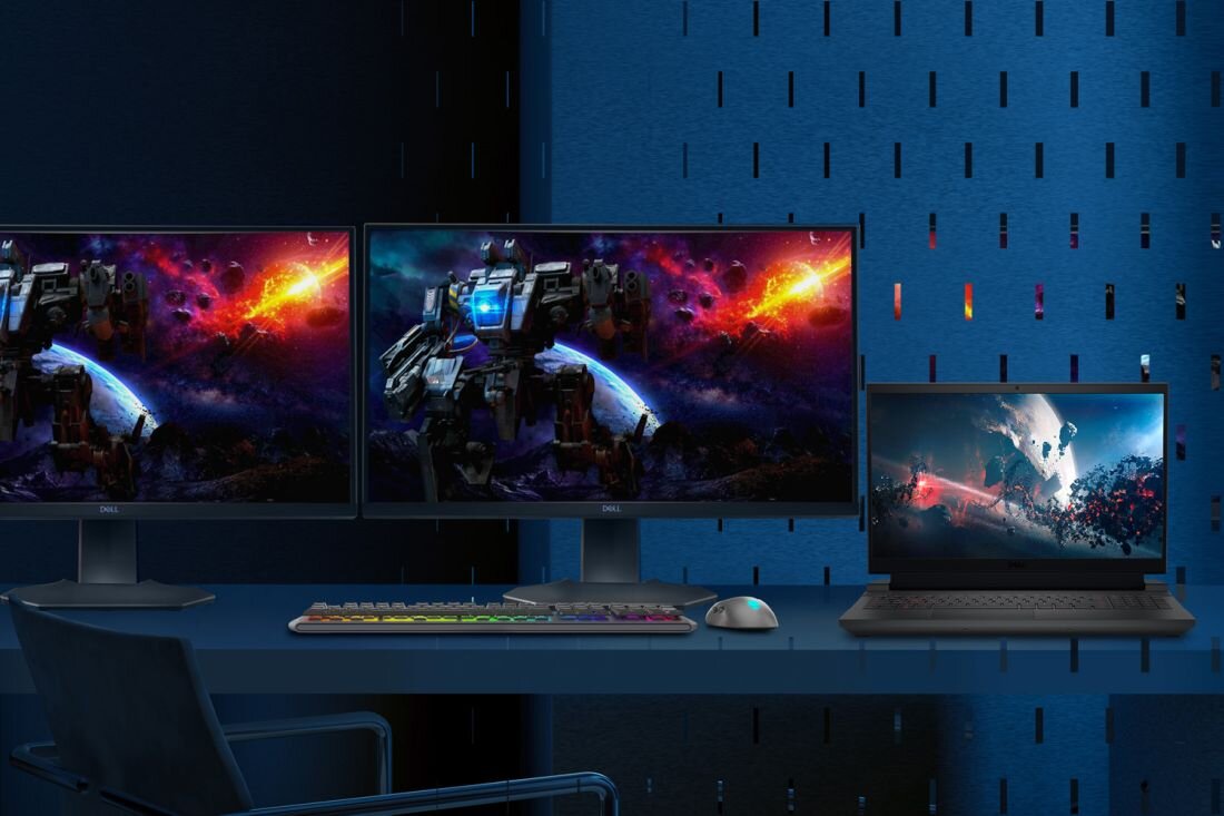 Na biurku znajdują się dwa monitory i laptop, wszystkie z wyświetlonymi kolorowymi grafikami science fiction. Obok laptopa leży klawiatura i myszka, a na monitorach widoczne jest logo \'DELL\'.
