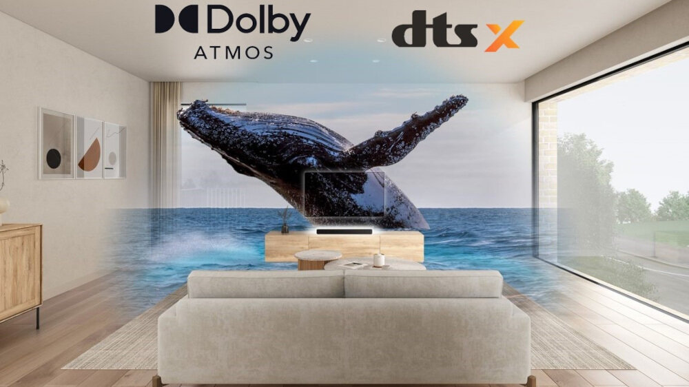 W salonie znajduje się telewizor z obrazem wieloryba wyskakującego z wody, a nad nim widoczne są loga \'Dolby Atmos\' i \'dts X\'. Przed telewizorem stoi szara kanapa, a obok znajduje się drewniana szafka.
