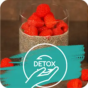 Szklanka wypełniona puddingiem chia z malinami na wierzchu. Na dole obrazu znajduje się turkusowy symbol z napisem \'DETOX\' i ikoną dłoni.