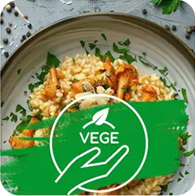 Na talerzu znajduje się danie z ryżem i grzybami, udekorowane zielonymi ziołami. Na obrazie widoczny jest zielony symbol z napisem \'VEGE\'.
