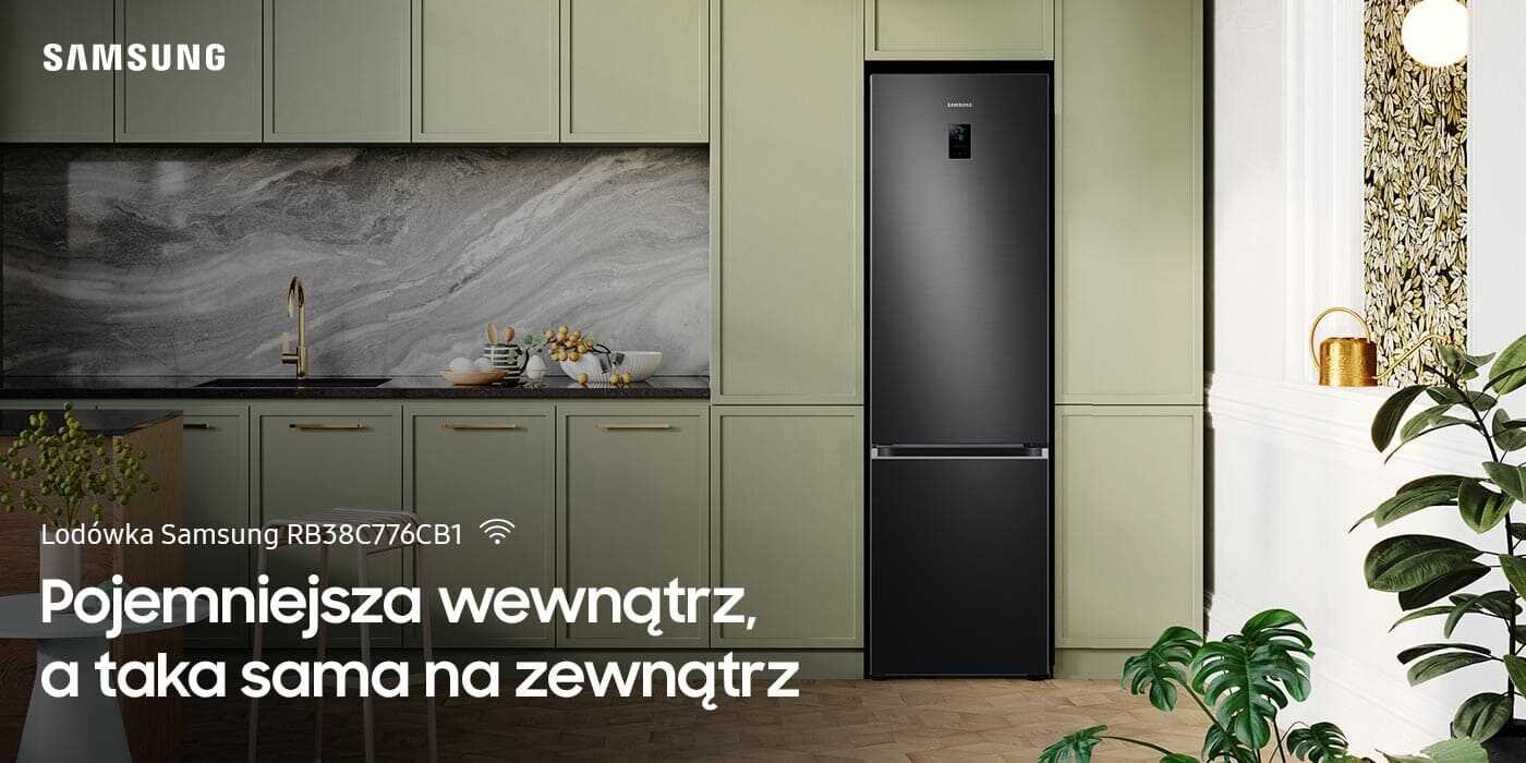 Dwudrzwiowa lodówka Samsung RB38C776CB1 z możliwością kontrolowania i obniżania zużycia energii elektrycznej z poziomu aplikacji, już dostępna w Media Expert Grafitowa lodówka stoi w eleganckiej kuchni z zielonymi szafkami i marmurowym blatem. Na obrazie widoczny jest tekst: \'Lodówka Samsung RB38C776CB1 Pojemniejsza wewnątrz, a taka sama na zewnątrz\'.