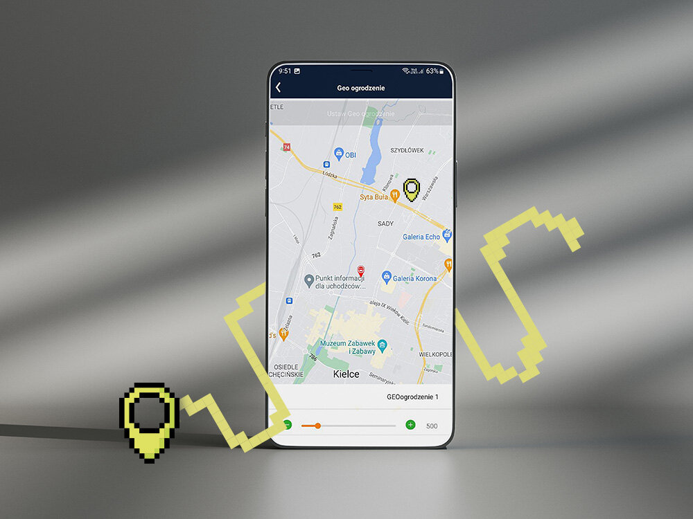 Na ekranie smartfona wyświetlona jest mapa z zaznaczonym punktem w okolicach Kielc oraz napis \'Geo ogrodzenie\'. Obok telefonu widoczna jest żółta, pikselowa ikona lokalizacji.