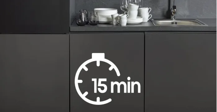 Na obrazie widać kuchnię z ciemnymi szafkami, na których stoi zestaw naczyń. Na szafce widoczny jest symbol zegara z napisem \'15 min\'.