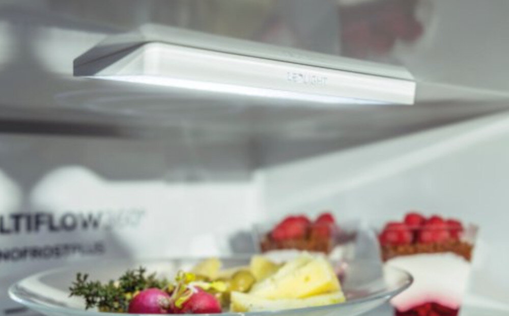 Wnętrze lodówki z widocznym oświetleniem LED i półką z jedzeniem, na której znajdują się owoce i deser. Na ścianie lodówki widoczny jest napis \'MULTIFLOW 360°\'.