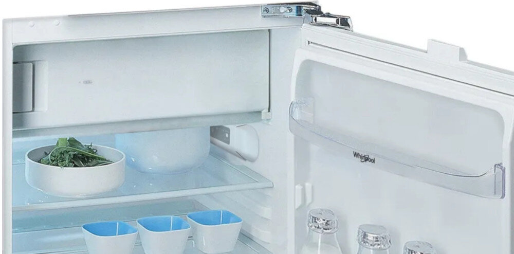 Wnętrze lodówki z widocznymi półkami, na których znajdują się naczynia i butelki. Na drzwiach widoczne jest logo \'Whirlpool\'.