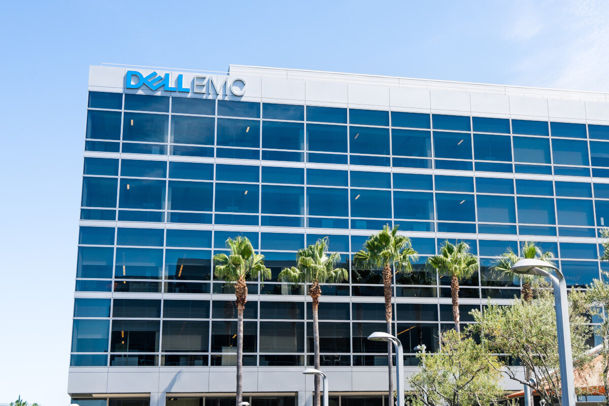 Budynek biurowy z dużymi oknami, na którym widnieje logo \'DELL EMC\'. Przed budynkiem rosną palmy i znajdują się latarnie uliczne.