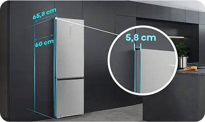 Srebrna lodówka w zabudowie z widocznymi wymiarami: 65,8 cm szerokości, 60 cm głębokości i 5,8 cm odległości od ściany. Obok na blacie kuchennym znajduje się deska z owocami.