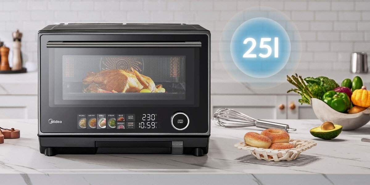 Na blacie kuchennym stoi kuchenka mikrofalowa z wyświetlaczem pokazującym 230°C i 10:59. Obok znajduje się miska z warzywami, trzepaczka i talerz z bułkami, a nad kuchenką widoczny jest napis \'25L\'.