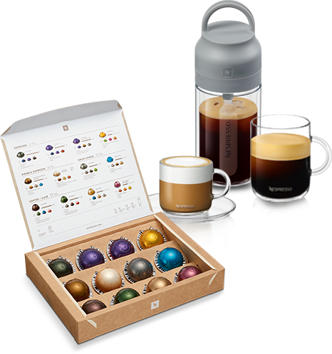 Na obrazie znajduje się otwarte pudełko z kapsułkami Nespresso w różnych kolorach oraz trzy filiżanki z kawą, z czego jedna jest przezroczysta z logo Nespresso. Obok znajduje się szary pojemnik z uchwytem, również z logo Nespresso.